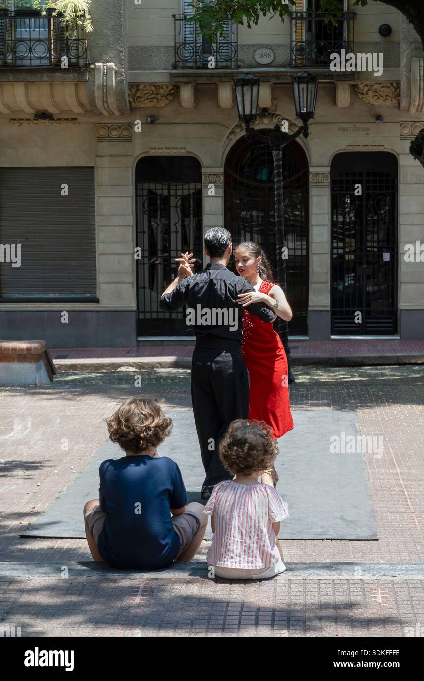 Due bambini piccoli guardano ballerini di tango per le strade di San Telmo, Buenos Aires, Argentina Foto Stock