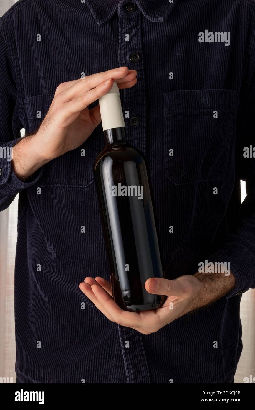 Mockup in bottiglia di vino di vetro scuro senza etichetta tenuto dalle mani dell'uomo. mockup di personalizzazione del marchio, presentazione online delle vendite di vini. crema indaco navy Foto Stock