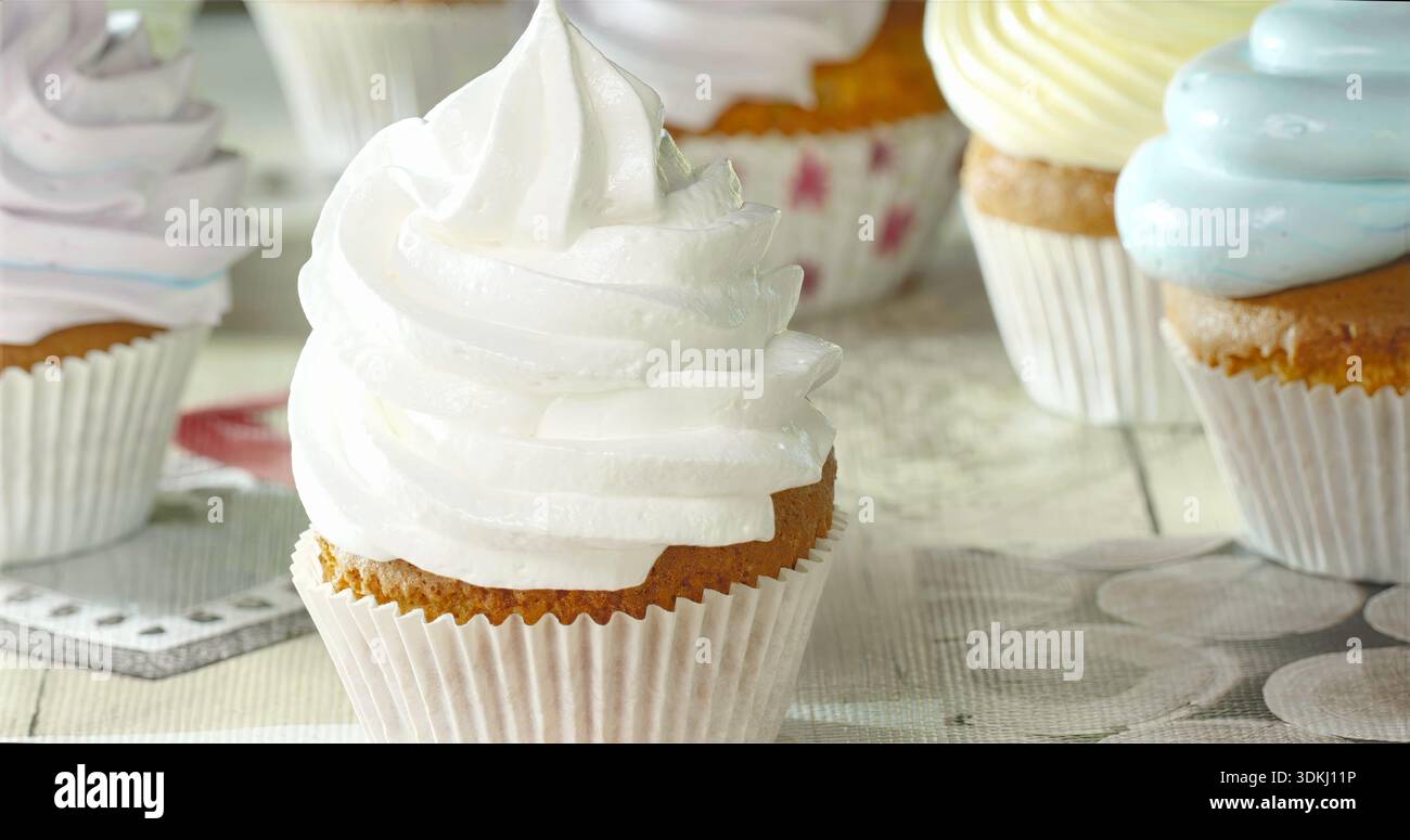 Cupcake alla vaniglia splendidamente decorata con glassa liscia su lino d'epoca in luce soffusa Foto Stock