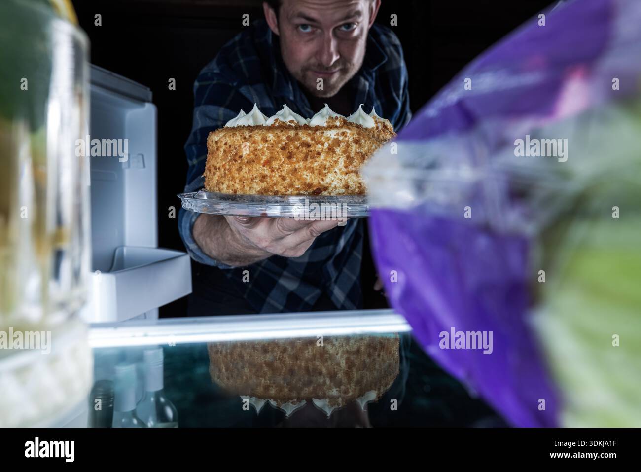 Un creativo punto di vista (POV) dall'interno di un frigorifero illuminato. L'immagine cattura l'espressione gioiosa di un uomo mentre lui Foto Stock