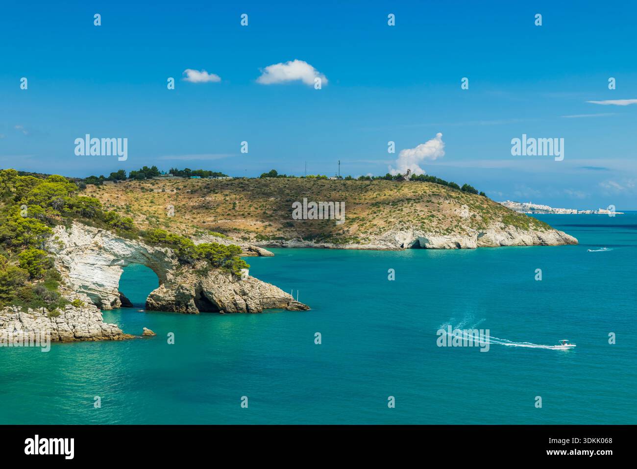 Arco di roccia naturale che si estende sul mare turchese con una barca che passa dalla costa di Vieste Foto Stock