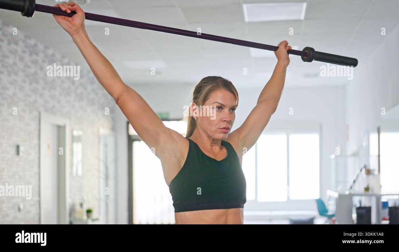 Donna che solleva il barbell sopra la testa durante la sessione di allenamento in palestra Foto Stock