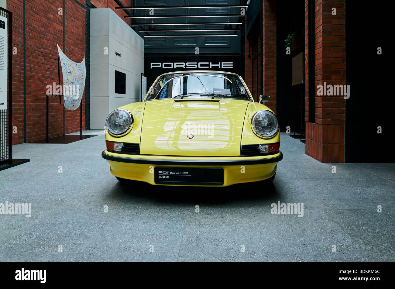 Ripresa simmetrica frontale Porsche gialla con cofano centrato e fari rotondi, cartellone museale e Varsavia lucida, Polonia 24-06-2025 Foto Stock