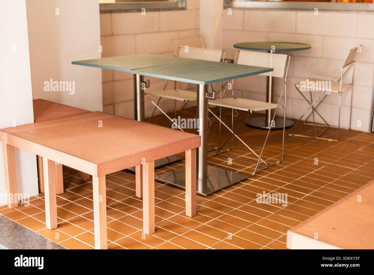 L'interno di una caffetteria presenta una configurazione semplice con tavoli e sedie. L'area presenta pavimento piastrellato e decor minimale, creando uno spazio per mangiare informale. Foto Stock
