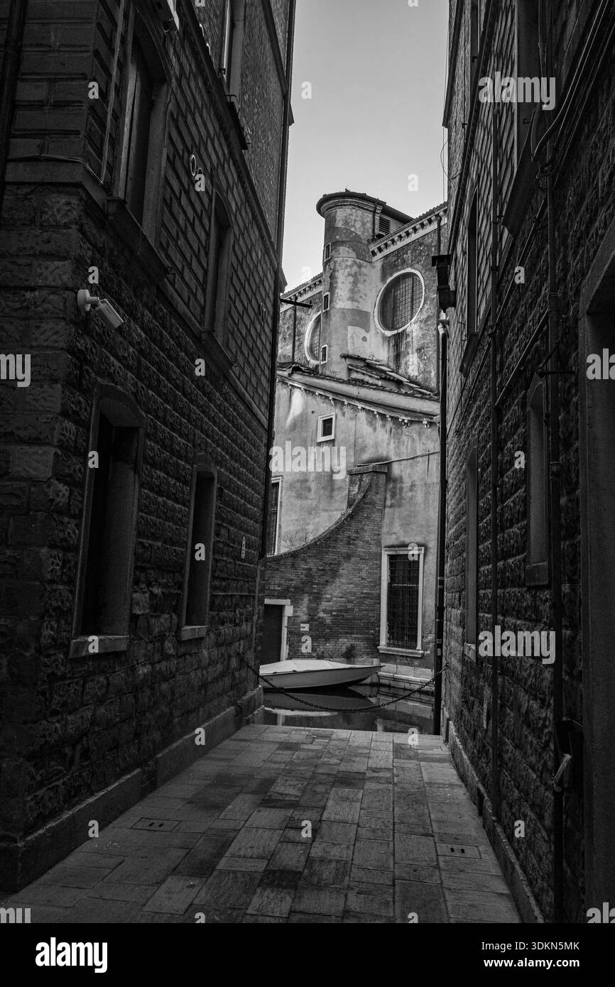 Venezia, Italia. 1° febbraio 2026. Uno stretto vicolo storico che conduce ad una chiesa di Venezia durante il periodo del Carnevale, mostrato in bianco e nero. Foto Stock