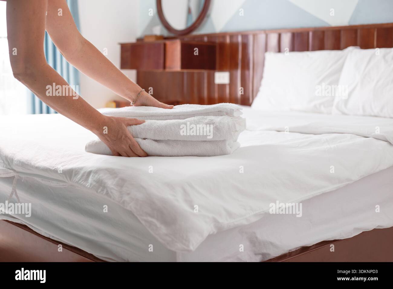 Le mani posizionano una pila di asciugamani bianchi piegati su un letto ben fatto in una camera d'albergo o in una pensione. Pulizia delle camere dell'hotel. Foto Stock