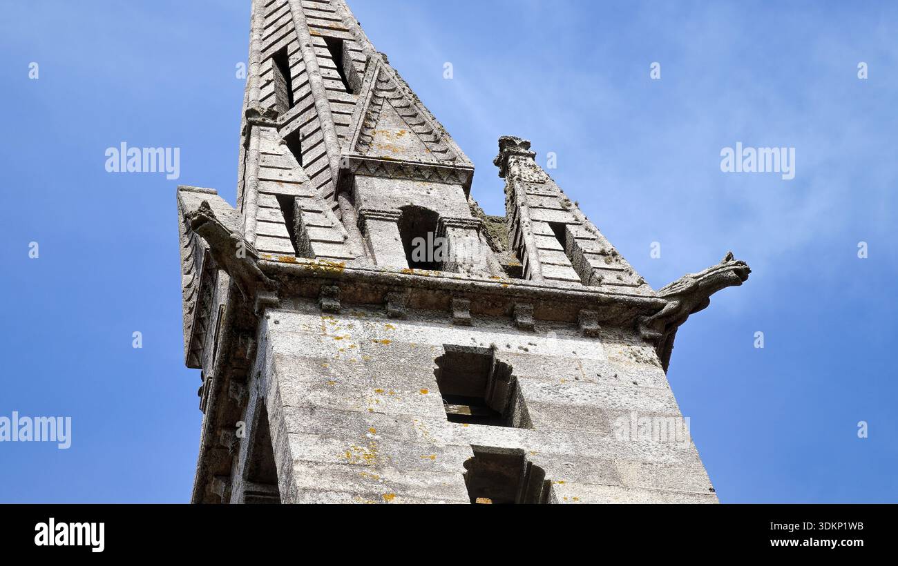 Una vista dettagliata di una torre storica della chiesa con una guglia di pietra intagliata in modo intricato contro un cielo blu brillante. Foto Stock