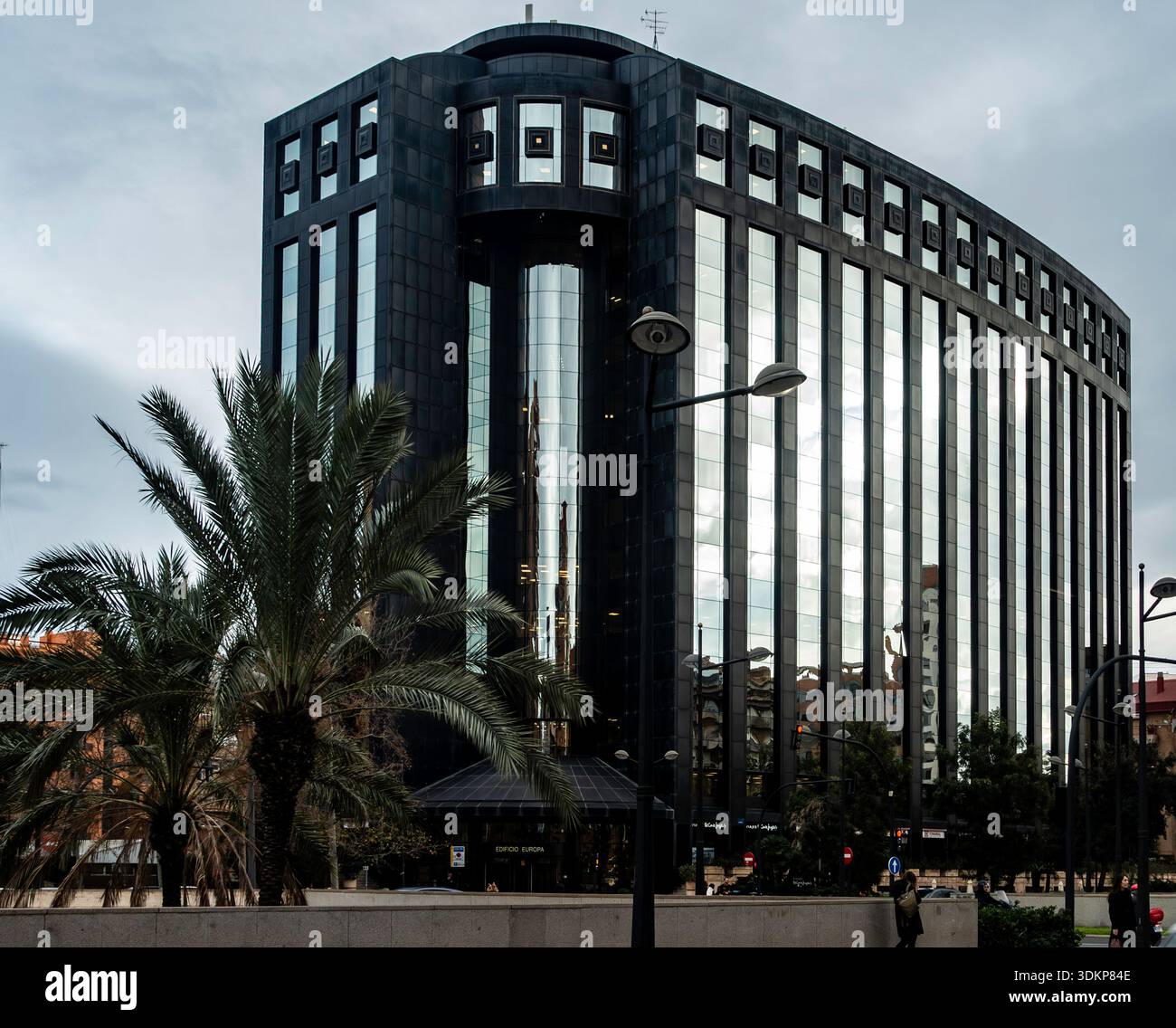 Il moderno edificio Europa di Valencia presenta una facciata in vetro scuro e riflettente e linee architettoniche curve distintive vicino a una strada fiancheggiata da palme. Foto Stock
