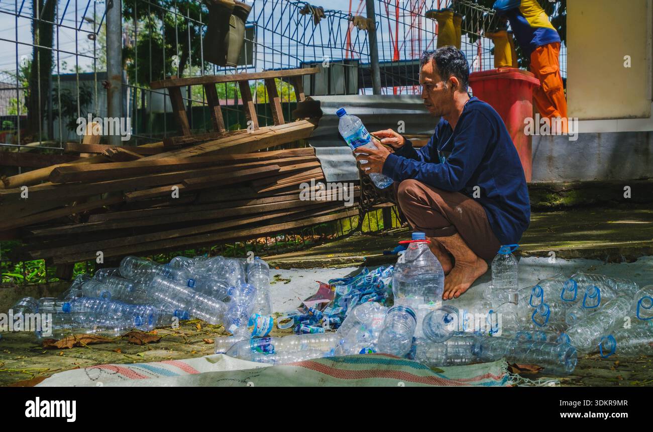 Balikpapan, Indonesia - 22 novembre 2025. Un lavoratore locale accovacciato durante lo smistamento delle bottiglie d'acqua in plastica scartate per il riciclaggio ambientale. Foto Stock