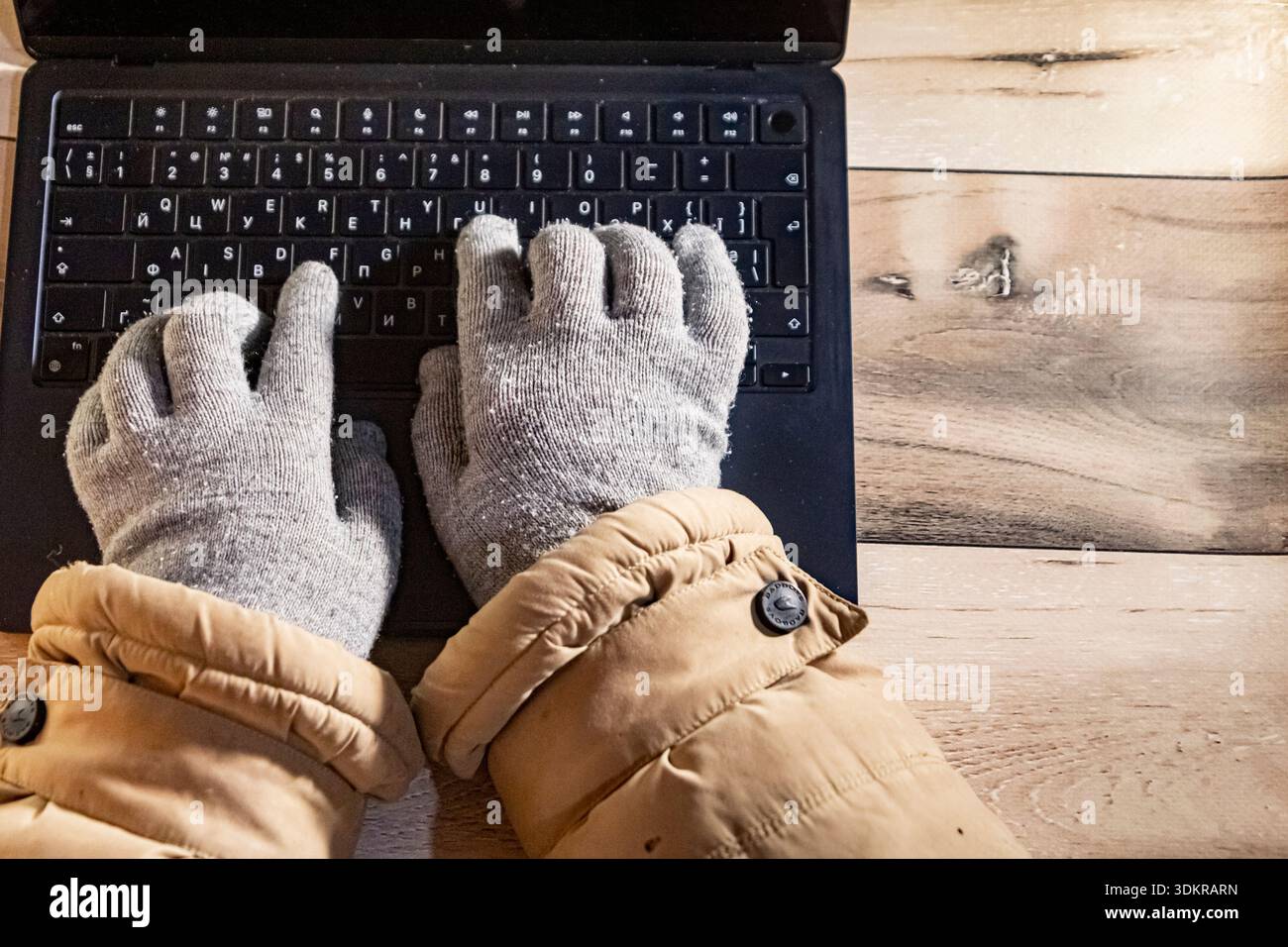 Vista dall'alto delle mani con guanti caldi che lavorano su un computer portatile a casa durante il blackout invernale in Ucraina, il lavoro a distanza, la vita freelance, l'adattamento al freddo Foto Stock