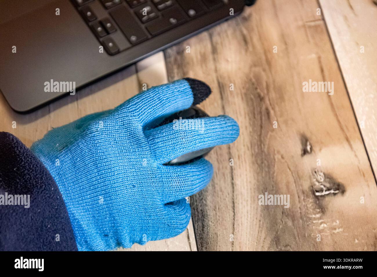 Vista laterale ravvicinata di una mano in un guanto blu con un mouse del computer durante il blackout invernale in Ucraina, che mostra il lavoro da remoto e lo stile di vita freelance Foto Stock