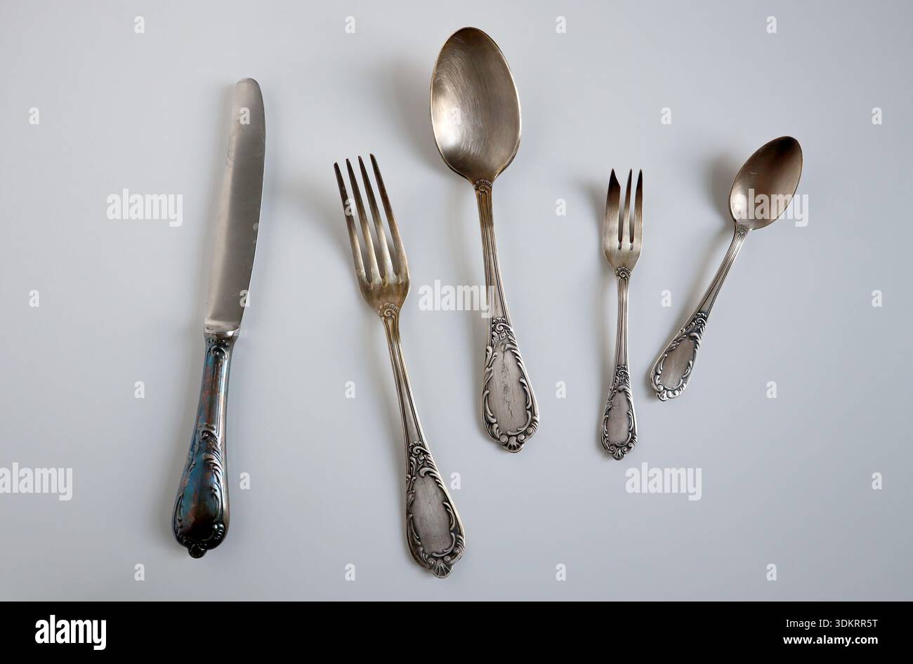 Set di posate vintage in nickel argento o Melchior con coltello, forchette, cucchiai su sfondo grigio chiaro. Vista dall'alto, disposizione piatta. Ideale per menu, antiquariato Foto Stock