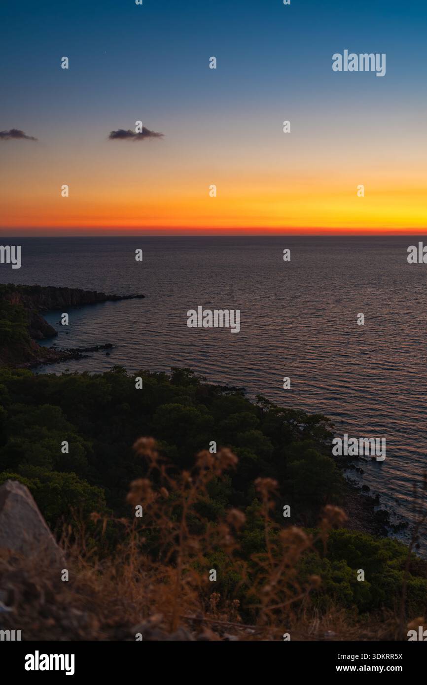 Tramonto colorato sul mare calmo e sul paesaggio roccioso della costa Foto Stock