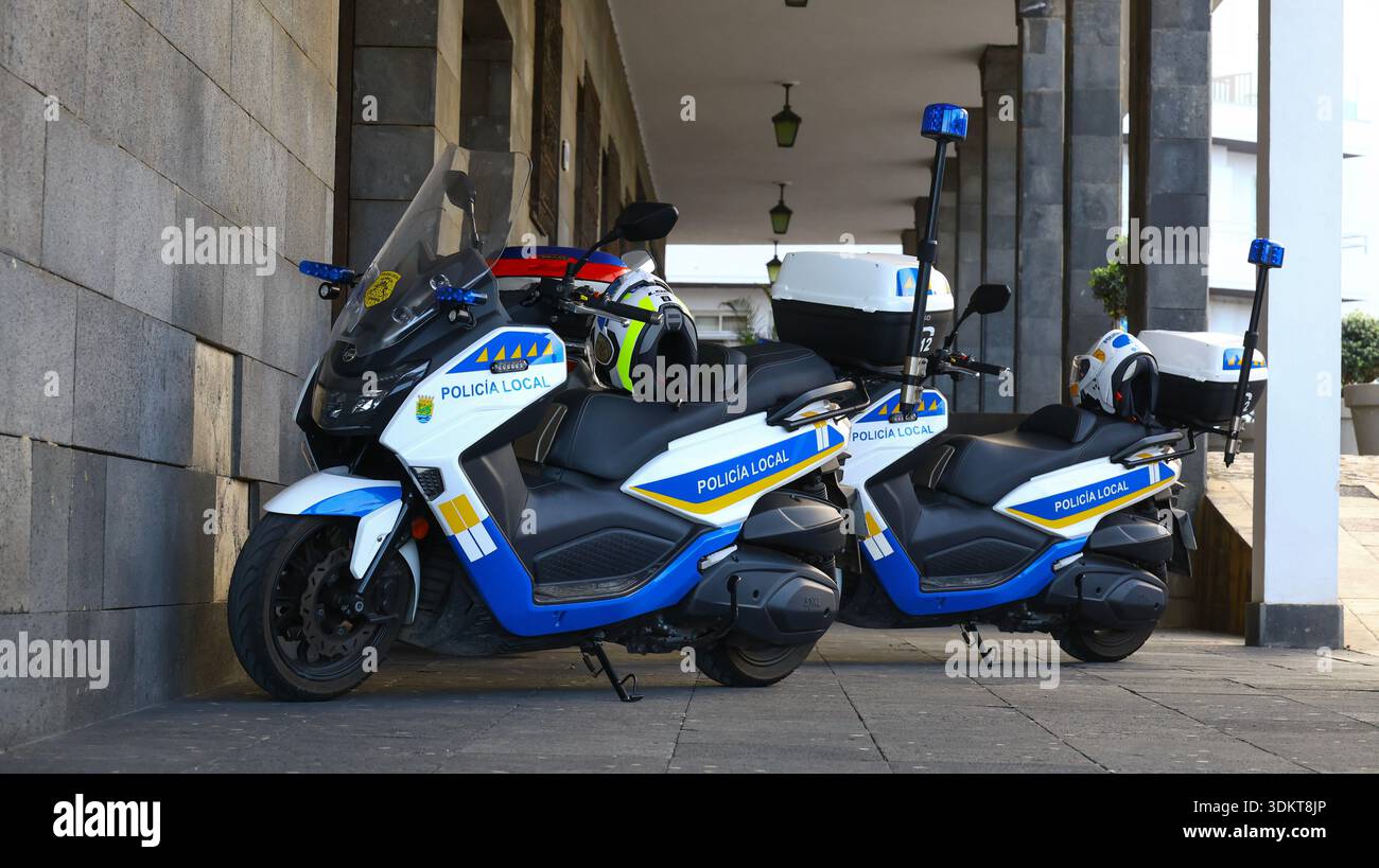 Puerto de la Cruz, Tenerife, 01152026 — due motociclette della polizia parcheggiate sotto un passaggio coperto in pietra, dotate di caschi, sirene e mezzi di comunicazione Foto Stock