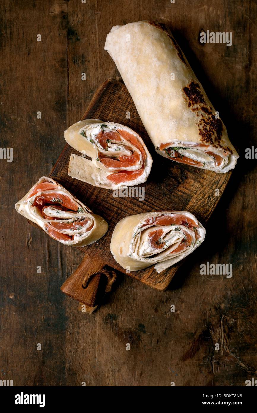 Salmone tagliato a fette con erbe di formaggio cremoso su un tagliere rustico in legno. Antipasto fresco con ripieno di panna di pesce. Foto Stock