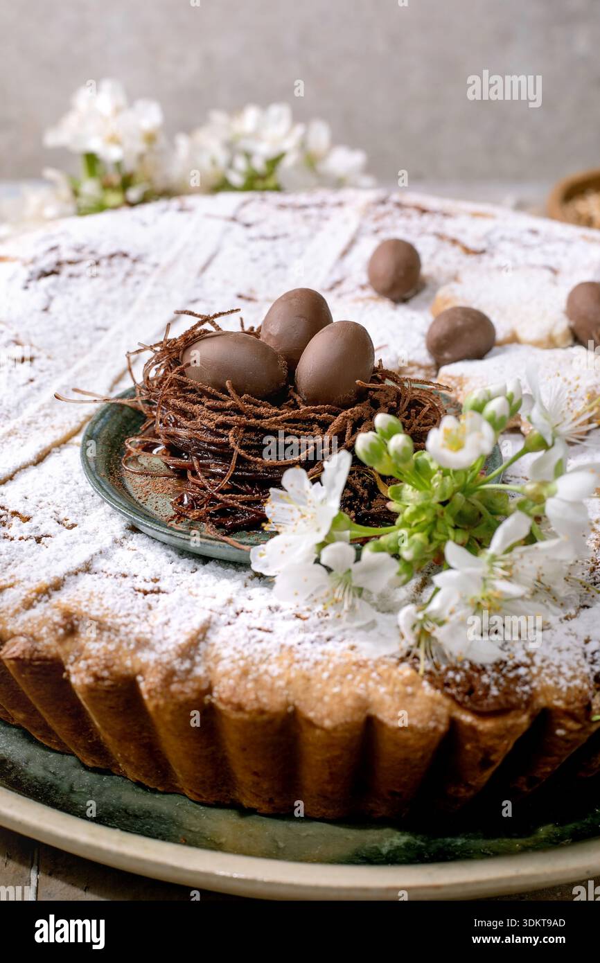 Torta pasquale fatta in casa Pastiera Napolitano con zucchero a velo ricoperto di nido di uova di cioccolato e fiori bianchi primaverili. Tradizionale dessert natalizio Foto Stock