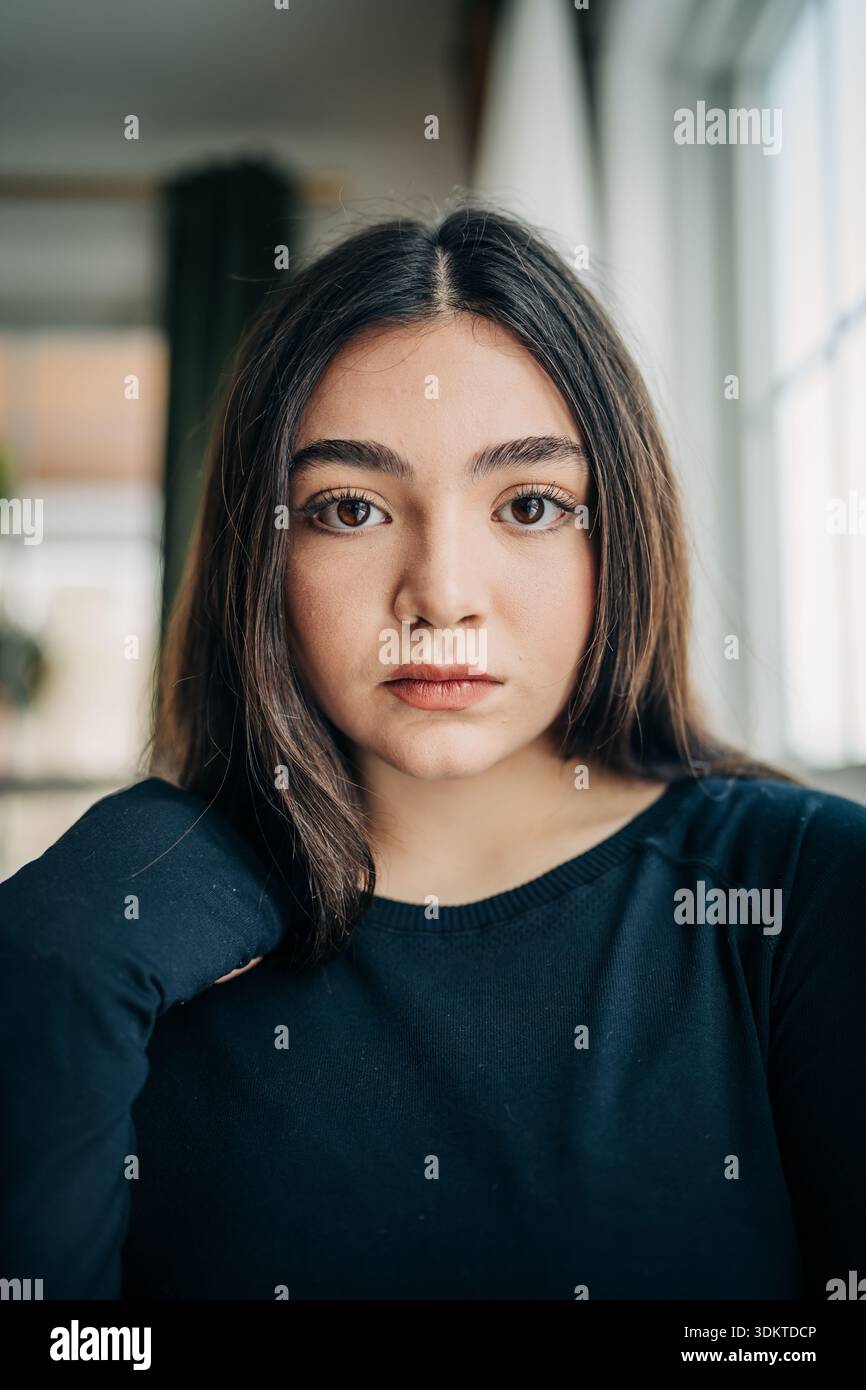 Giovane donna in cima nera che guarda seriamente sotto la luce naturale Foto Stock