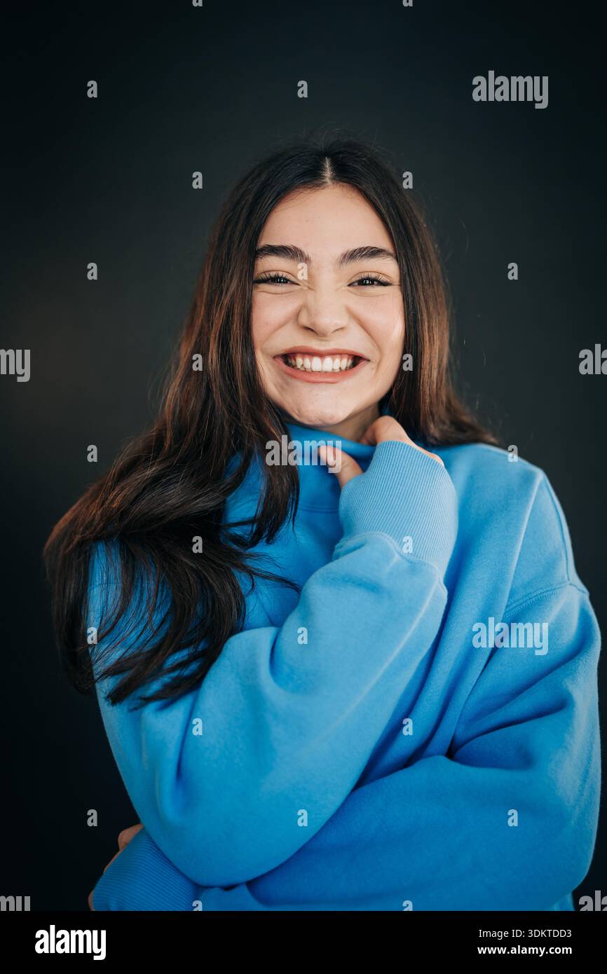 Giovane donna sorridente mentre indossa una felpa blu Foto Stock