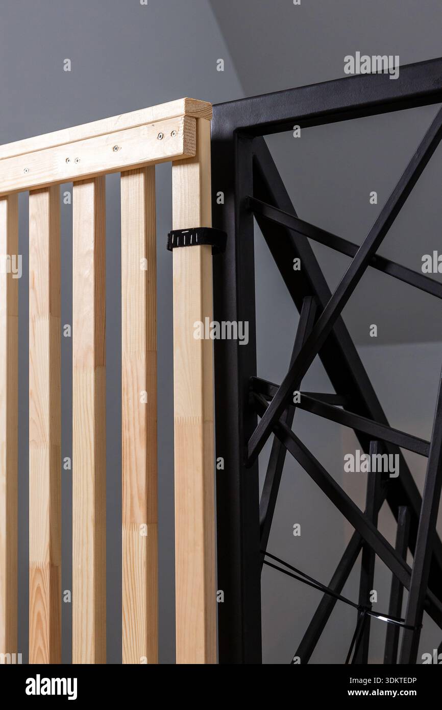 Vista dettagliata di una struttura a doghe in legno con struttura in metallo nero con design angolari, fissata da un fermo in plastica nera sotto un'illuminazione soffusa. Foto Stock