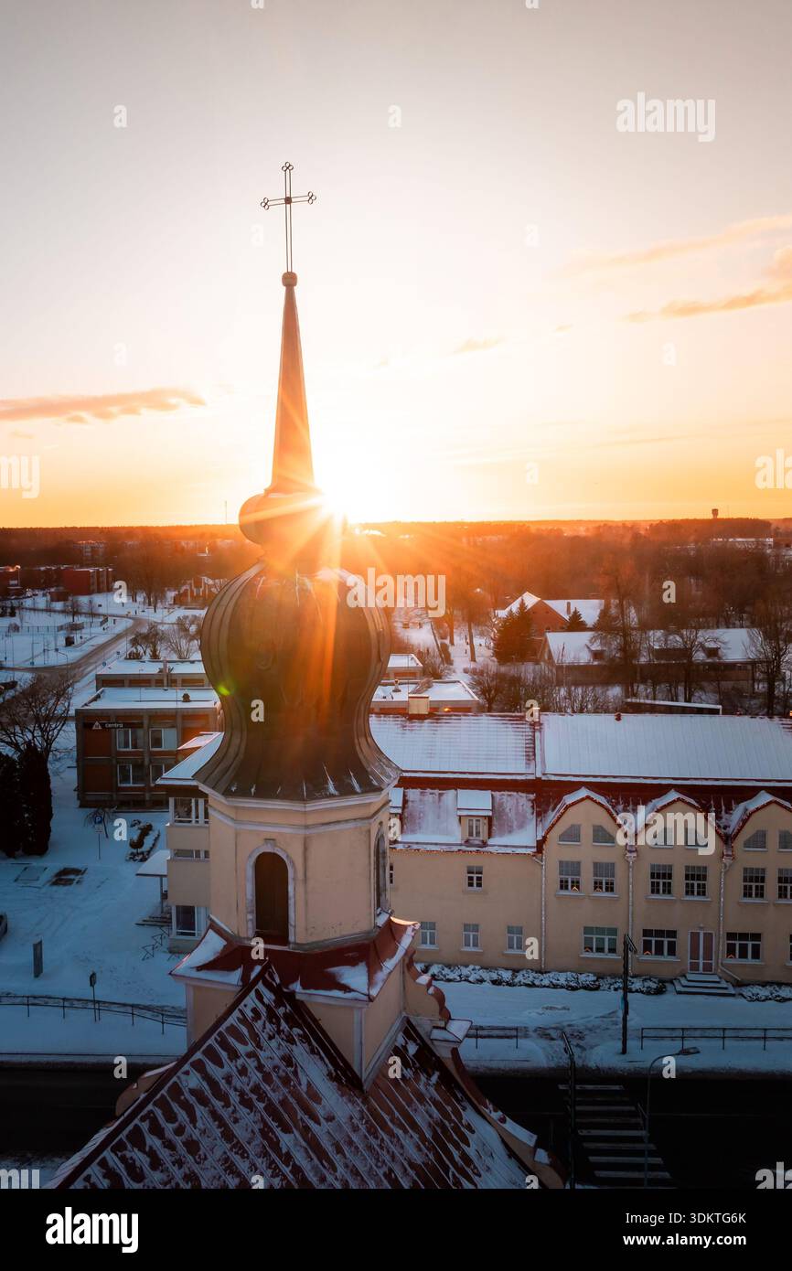 Una chiesa con una cupola a forma di cipolla e croce è illuminata dalla luce dorata del sole. La neve copre gli edifici e le strade circostanti in un ambiente invernale. Foto Stock