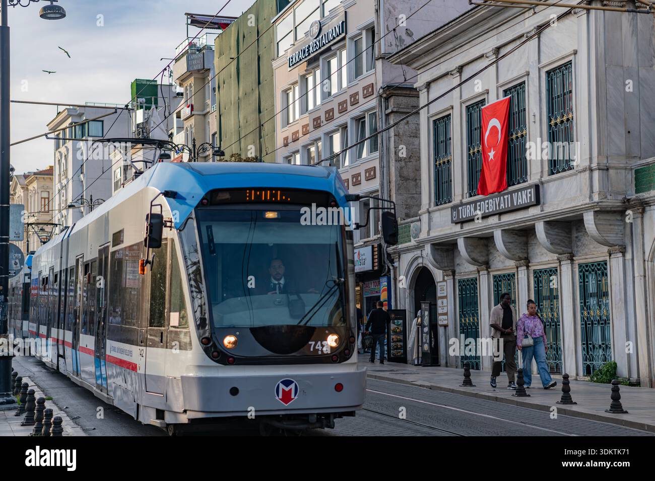Istanbul, Turchia - 31 ottobre 2025: Un moderno tram blu attraversa l'edificio della Fondazione della Letteratura turca nell'area di Sultanahmet. Foto Stock