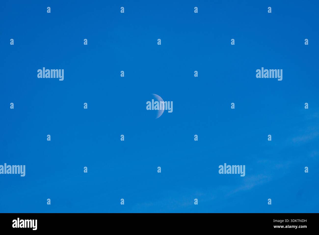 Vista minimalista di una mezza luna che galleggia in un chiaro cielo blu diurno. Foto Stock