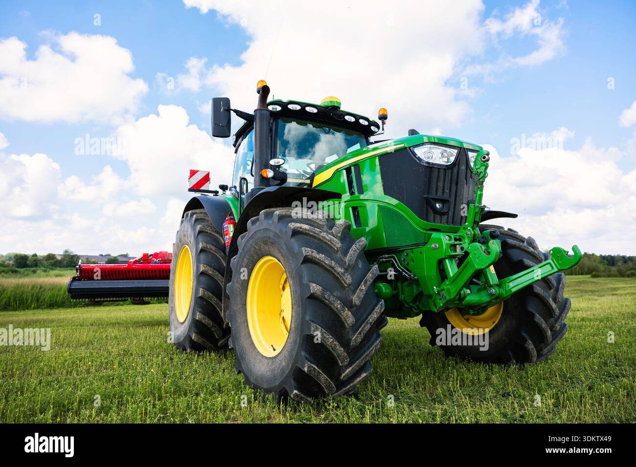 Trattore John Deere luminoso con battistrada profondi e cerchioni gialli abbassato, sollevatore anteriore idraulico visibile, cupola GPS sulla cabina, attrezzo rosso agganciato, c Foto Stock
