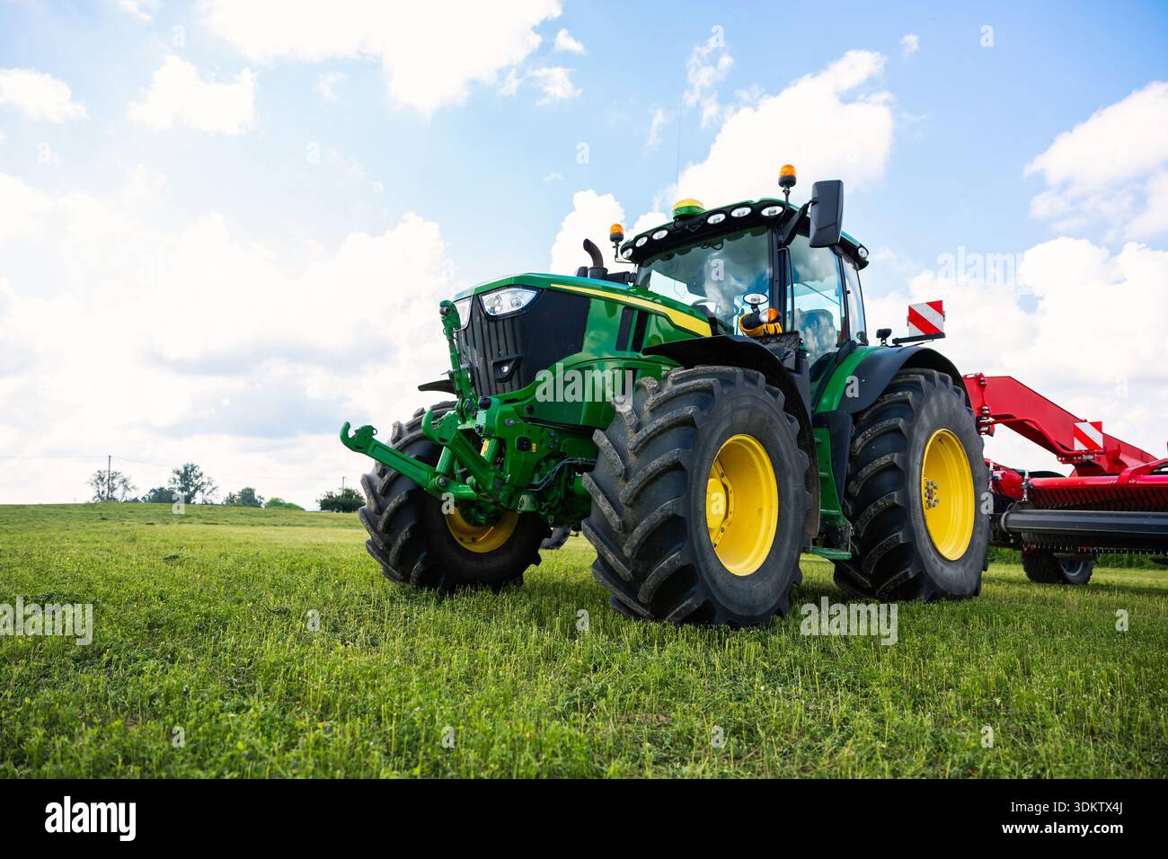 Trattore John Deere verde brillante con pneumatici con battistrada e rasaerba rosso su pascolo corto, che mostra il sollevatore idraulico, la cupola GPS e i girofari di sicurezza in r Foto Stock