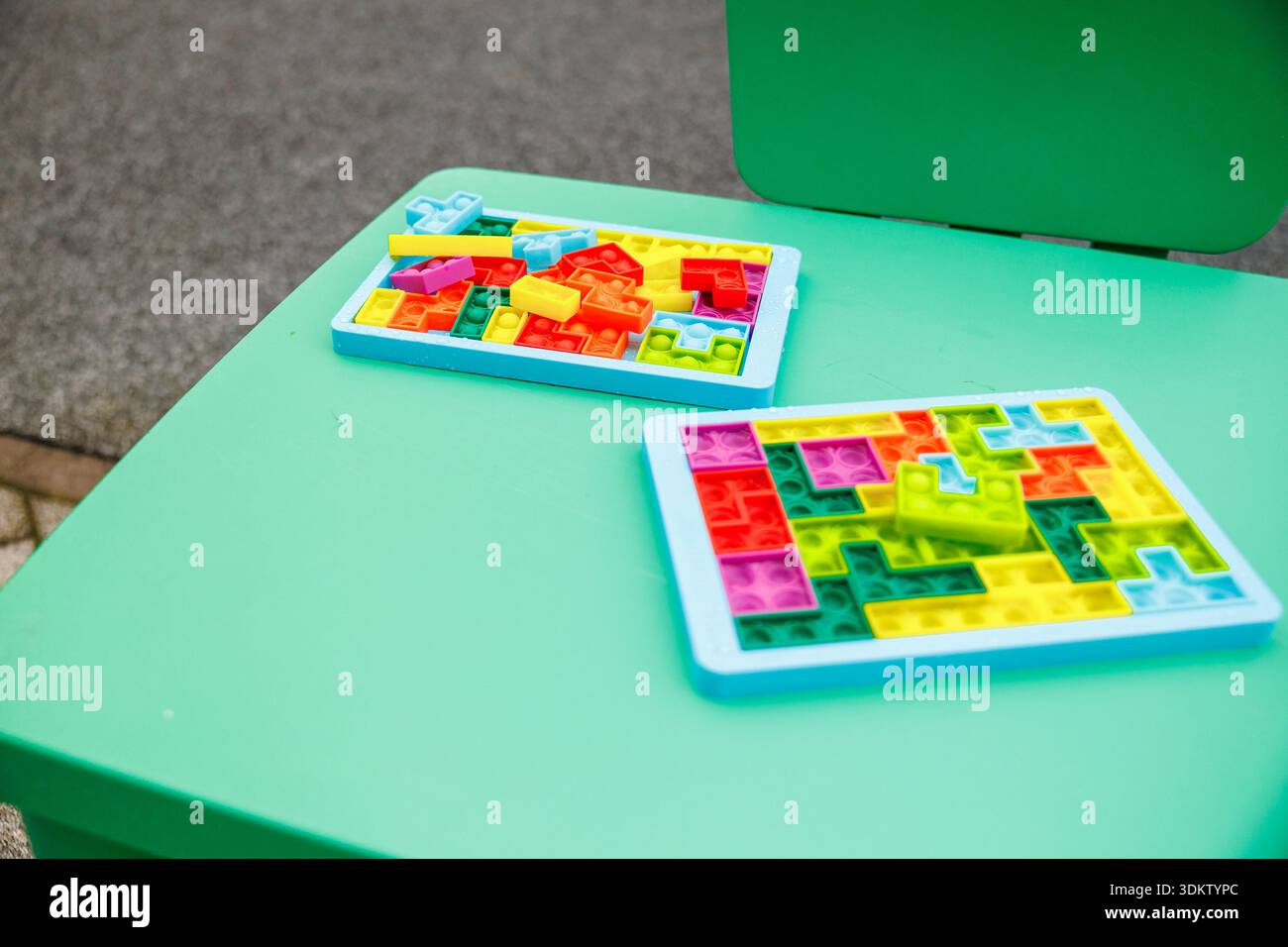 Due vassoi puzzle di plastica sono posizionati su un tavolo di menta, uno completo e uno con pezzi sparsi. Le bolle in silicone e i toni vivaci si distinguono per la morbidezza del colore naturale Foto Stock