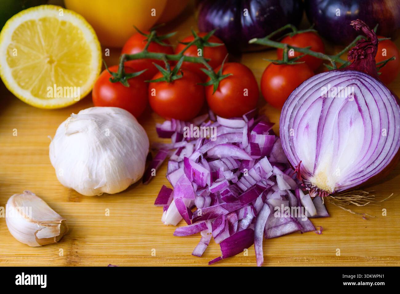 Cipolla rossa tritata con aglio, pomodori ciliegini e limone su un tagliere di legno. Ingredienti sani di primavera per cucinare, insalate e salse. Foto Stock