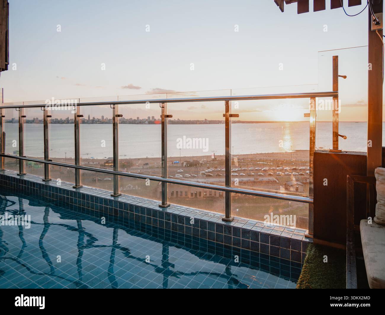 Immagine di una piscina in primo piano con una ringhiera di vetro e il mare sullo sfondo, illuminato dalla calda luce del tramonto. Ideale per il ballo Foto Stock
