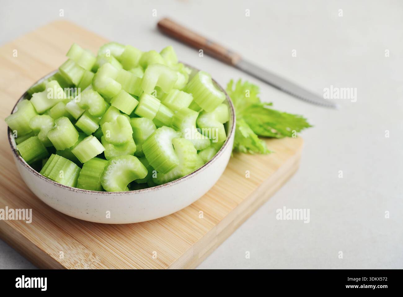 Сhopped gambi di sedano fresco in una ciotola su un tagliere di bambù, primo piano Foto Stock