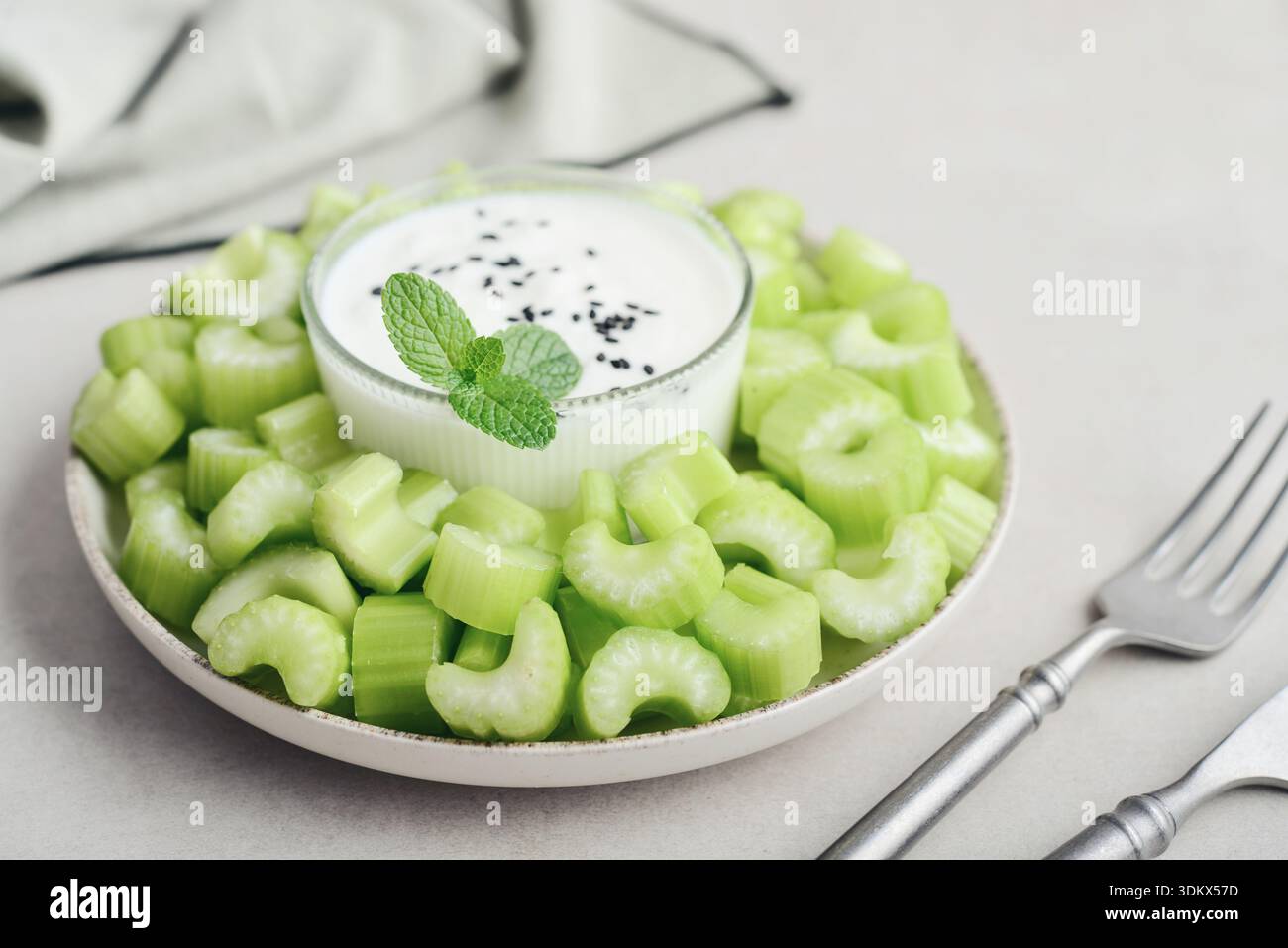 Gambi di sedano tritati con yogurt greco in una ciotola su un tagliere di bambù, primo piano Foto Stock