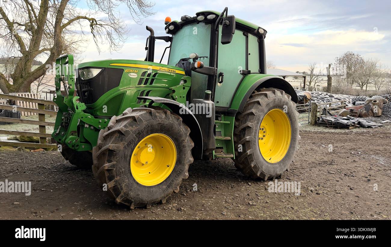 Un moderno trattore verde john deere parcheggiato in un'azienda agricola, circondato da alberi e attrezzature agricole, che mette in mostra macchinari agricoli in azione Foto Stock