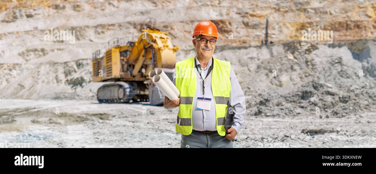Ingegnere con un giubbotto di sicurezza e un elmetto che reggono i progetti su un pozzo minerario Foto Stock