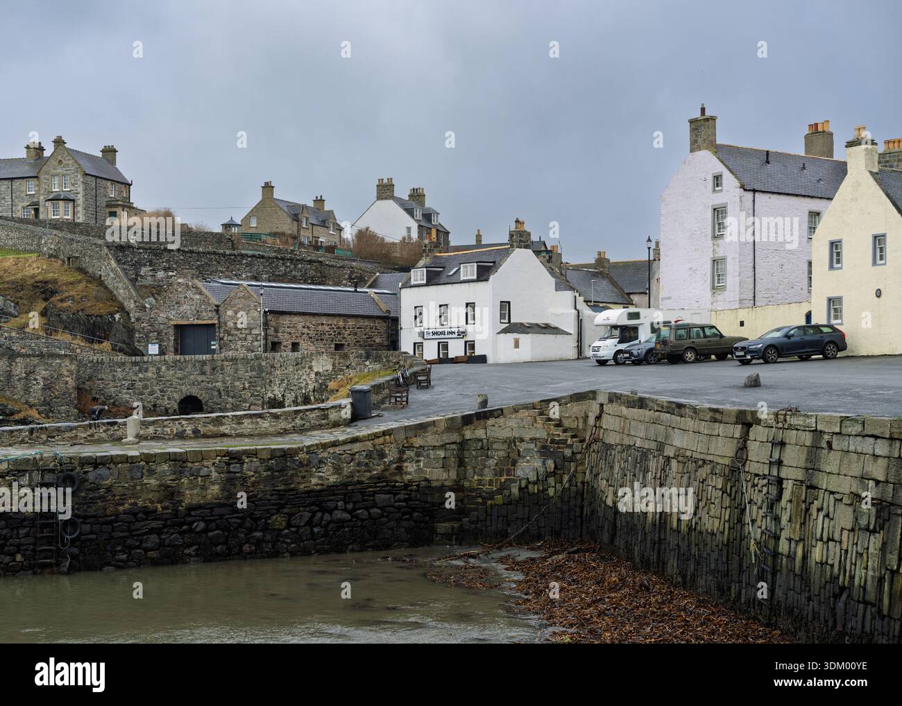 Vecchi edifici in pietra e case dipinte di bianco creano una strada panoramica nella città di pescatori di Portsoy. Le auto sono parcheggiate presso lo Shore Inn e le mura del porto incontrano tr Foto Stock
