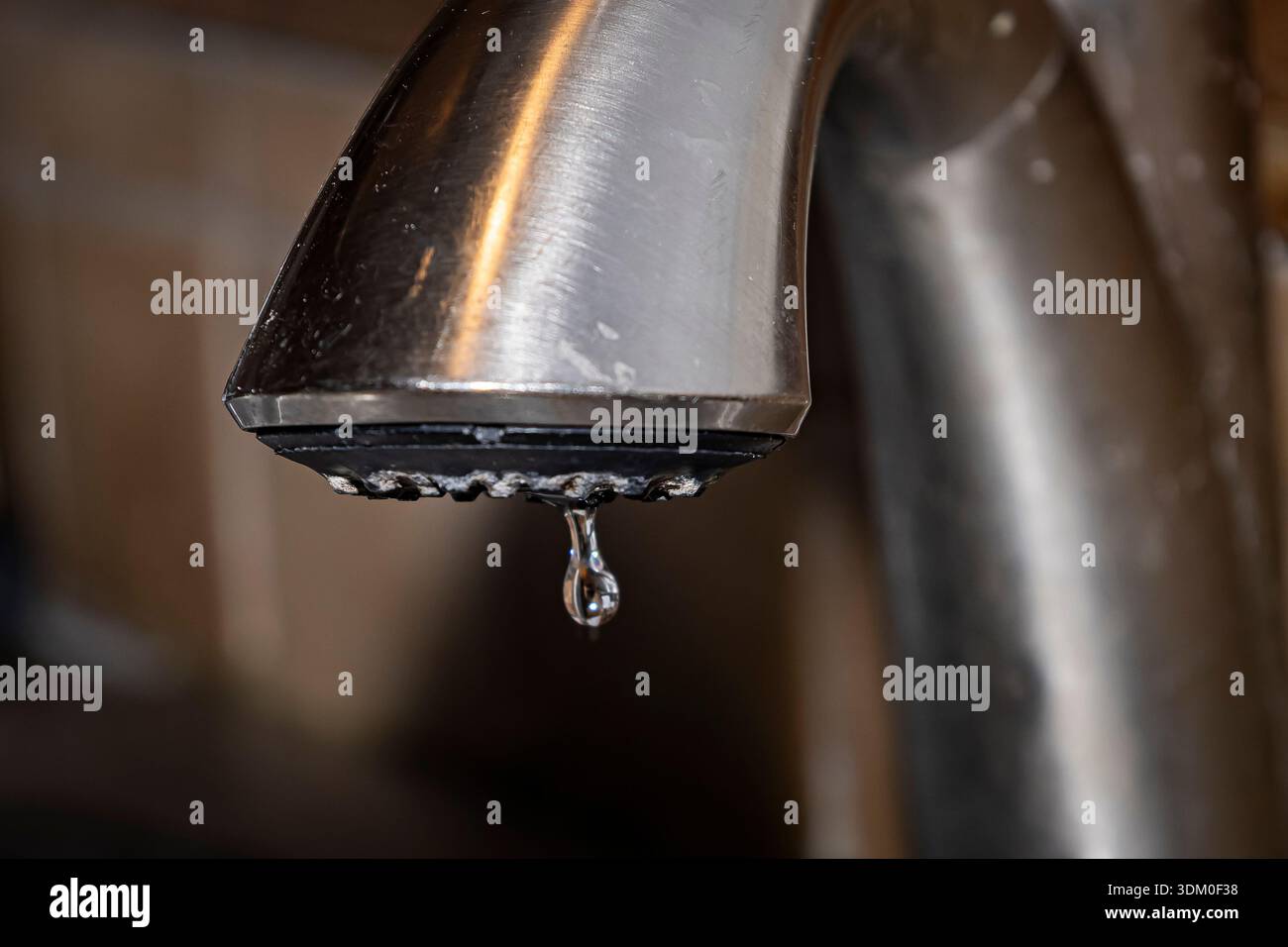 Primo piano di una singola goccia d'acqua che cade da un rubinetto da cucina in metallo spazzolato con depositi minerali visibili e accumuli di calcare. Foto Stock