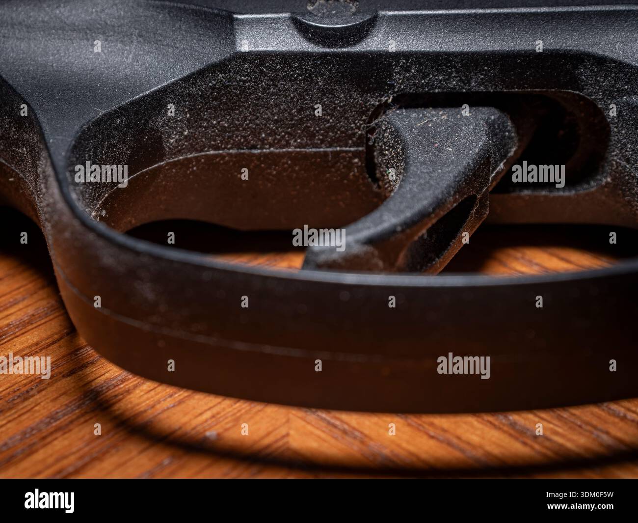 Primo piano macro estremo di un grilletto di un'arma da fuoco in polimero nero e di una protezione del grilletto, che mostra particelle di polvere fini e consistenza meccanica su una superficie in legno. Foto Stock