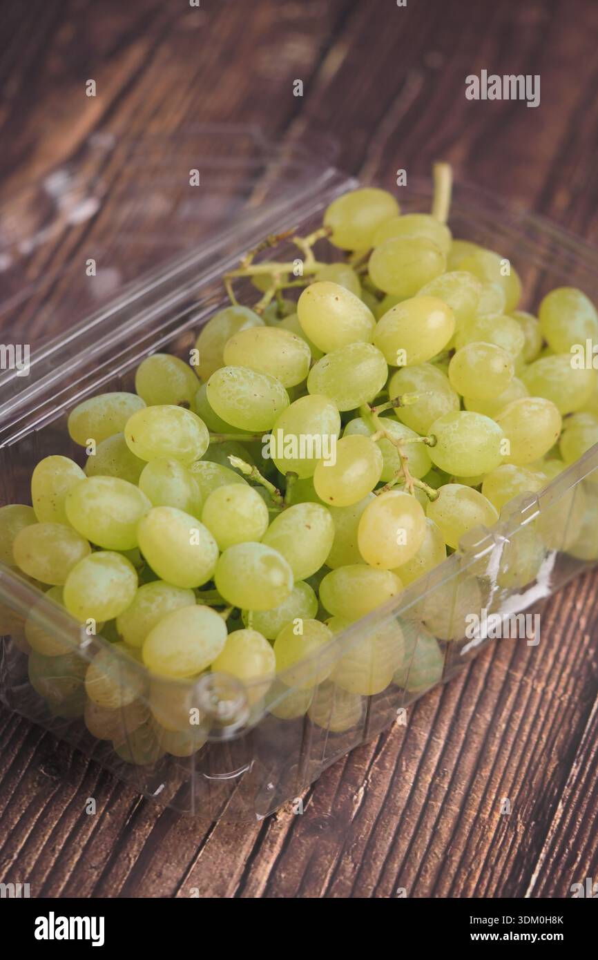 Uva verde fresca in un contenitore di plastica trasparente su legno Foto Stock