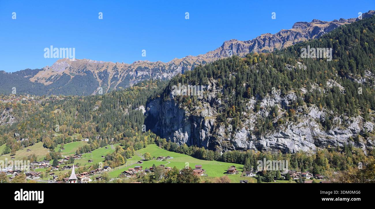 Paesaggio alpino con scogliere boscose, pareti rocciose calcaree e una valle verde sotto un cielo blu cristallino, che mostra un'elevazione spettacolare Foto Stock