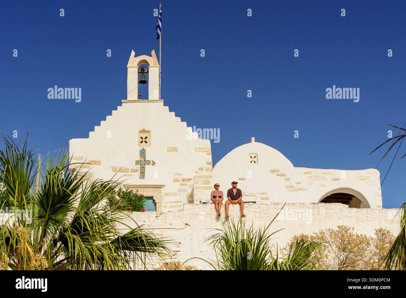 La coppia si siede sul vecchio muro di fronte alla Chiesa di San Costantino bagnata dal sole del tardo pomeriggio, Parikia, Paros, Cicladi, Grecia Foto Stock