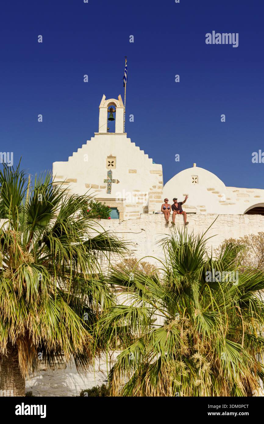 La coppia si siede sul vecchio muro di fronte alla Chiesa di San Costantino bagnata dal sole del tardo pomeriggio, Parikia, Paros, Cicladi, Grecia Foto Stock