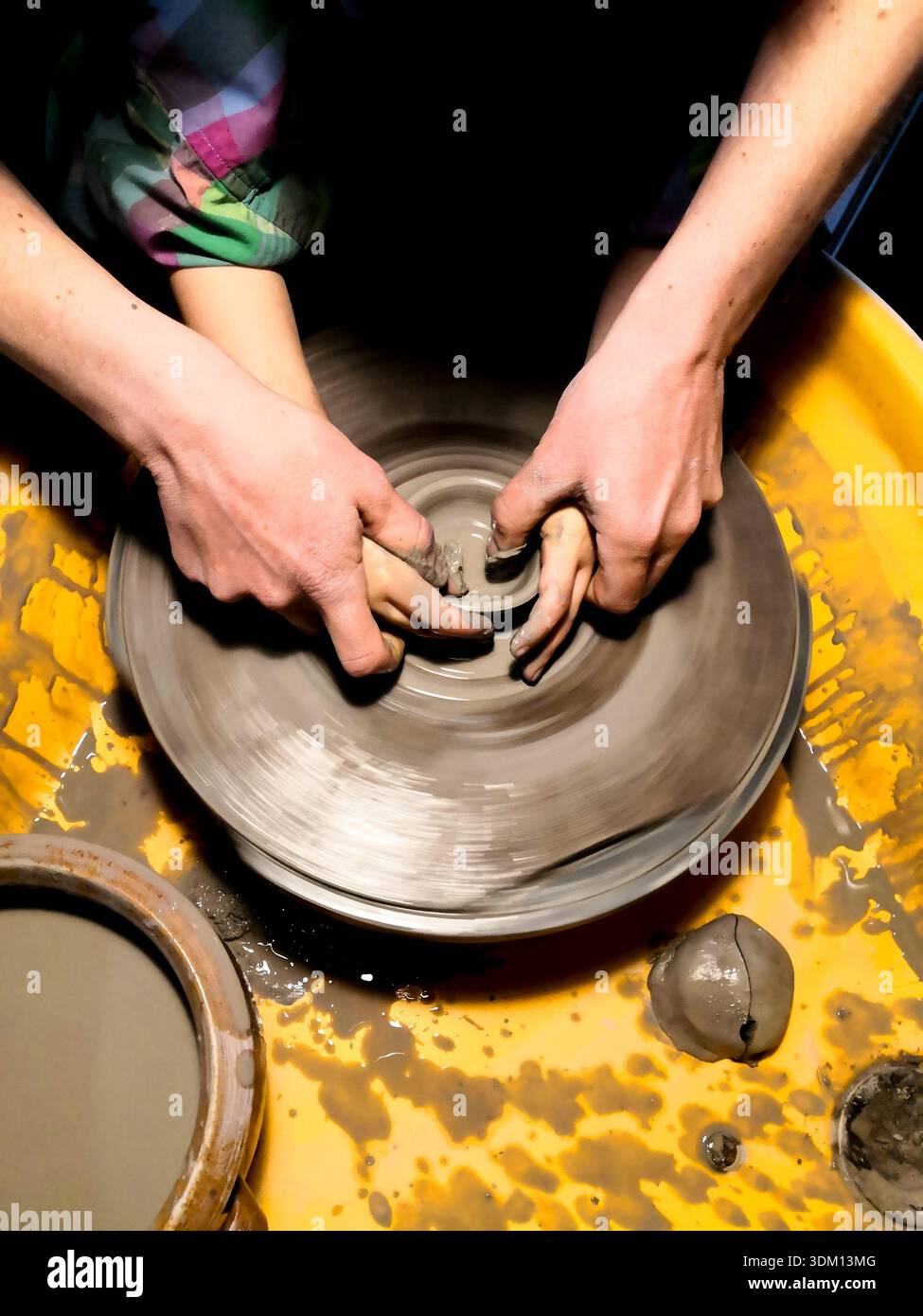 Mani adulte che guidano le mani dei bambini mentre modellano l'argilla bagnata su una ruota di ceramica, illustrano l'apprendimento, la guida e l'artigianato tradizionale della ceramica, Foto Stock