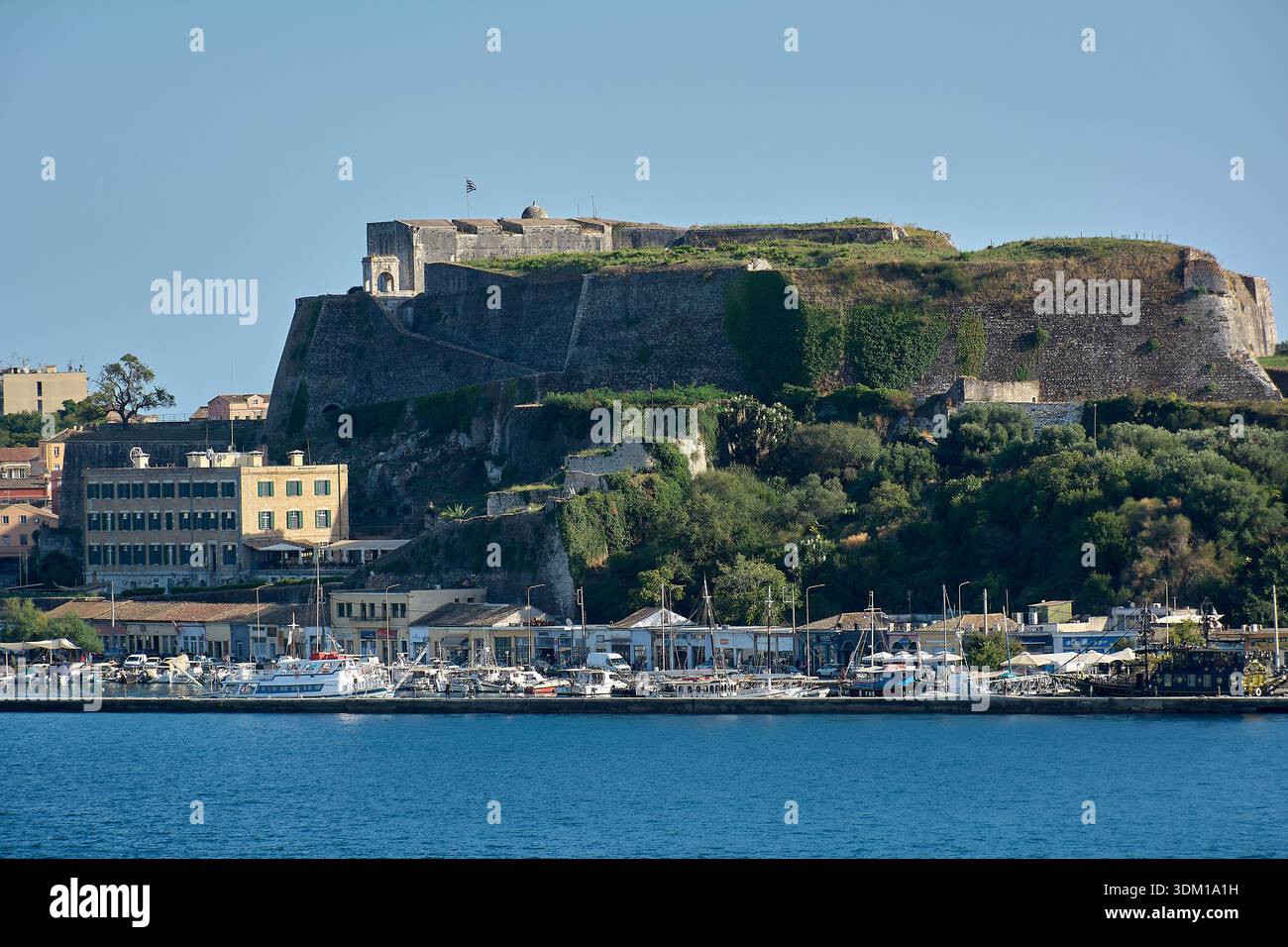 Corfù. Grecia - 3 febbraio 2026: Paesaggio urbano costiero panoramico con collina fortificata, architettura tradizionale e porto funzionante, che esprimono l'isola Foto Stock
