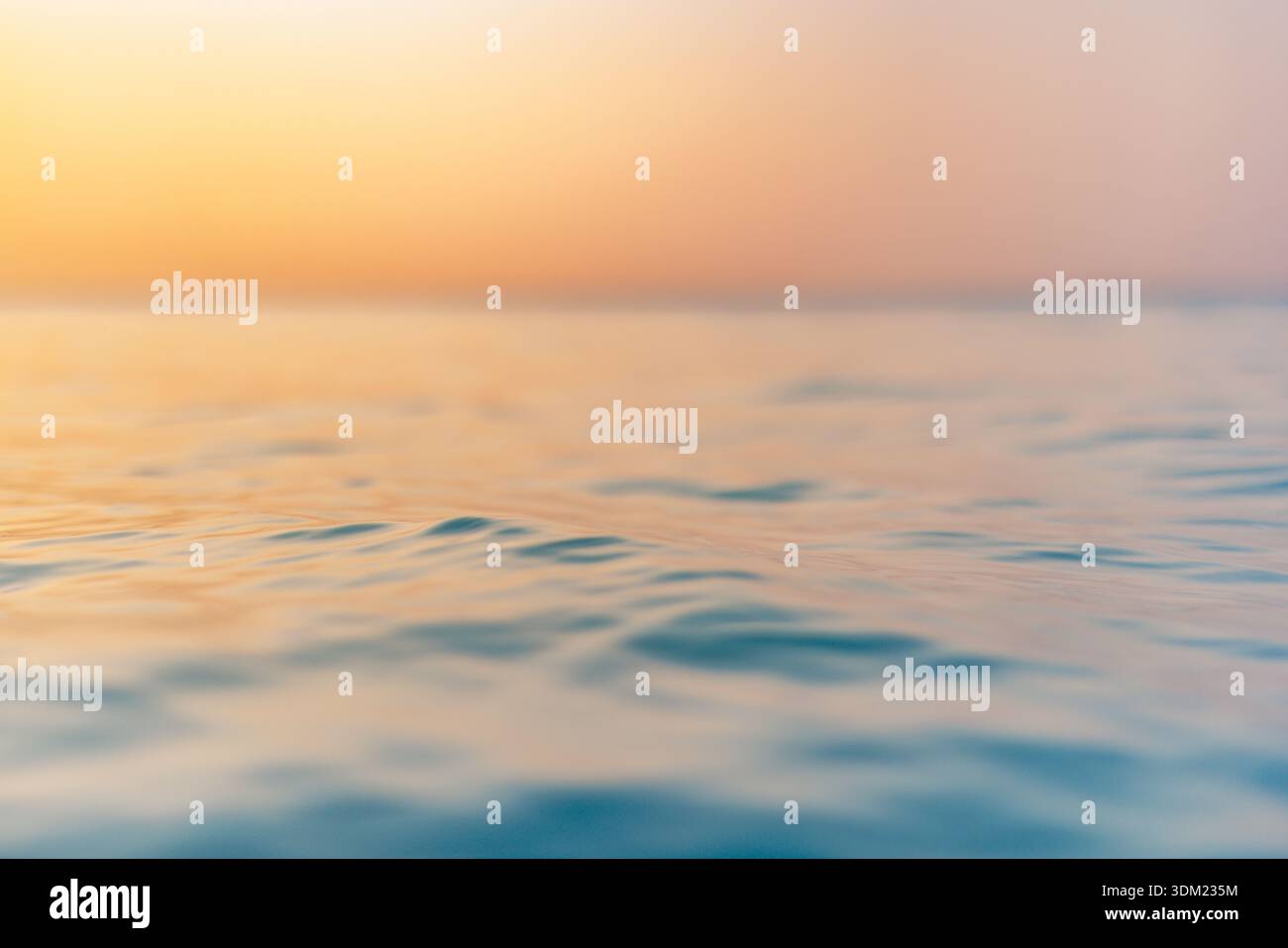 Splendida e tranquilla superficie dell'oceano, orizzonte caldo e dorato al tramonto, serene, tranquille e sognanti, onde dolci che illuminano il paesaggio marino e un liquido tranquillo Foto Stock