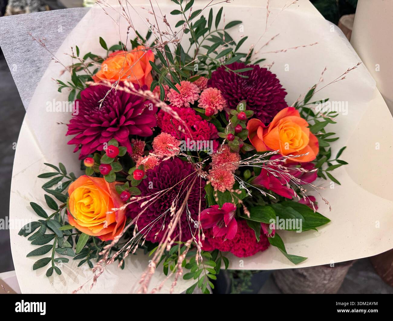 Luminoso bouquet floreale autunnale con rose arancioni, crisantemi Bordeaux, garofani e bacche di hypericum Foto Stock