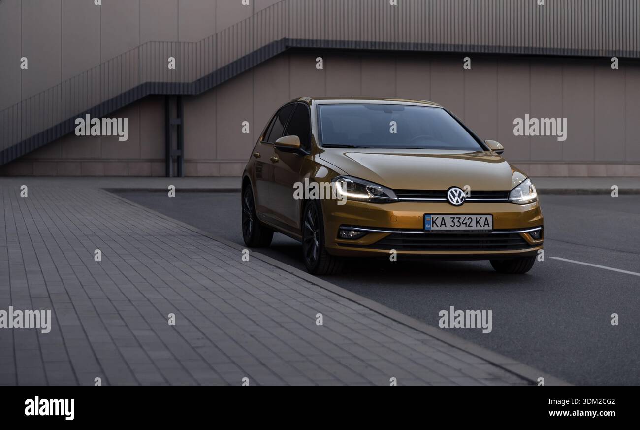 Campo da golf Amber VW di fronte al muro beige. Vista anteriore di tre quarti della berlina Volkswagen in un ambiente urbano, parcheggiata vicino a un marciapiede e a una parete color beige. Foto Stock