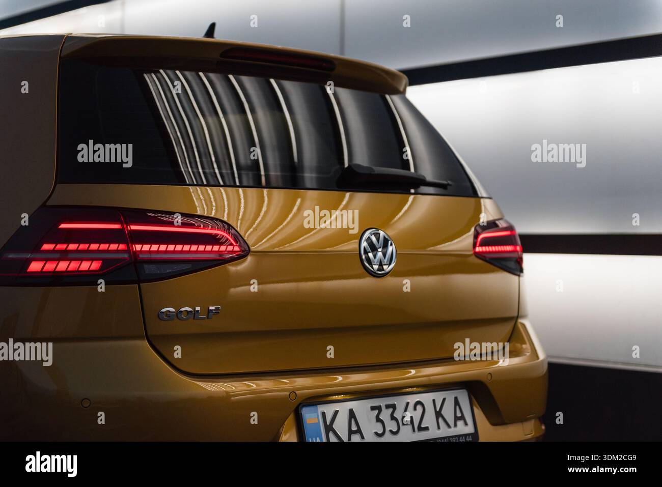 Campo da golf Amber Volkswagen su una strada con un muro luminoso bianco. Parte posteriore della moderna berlina con luci di coda a LED accese. Foto Stock