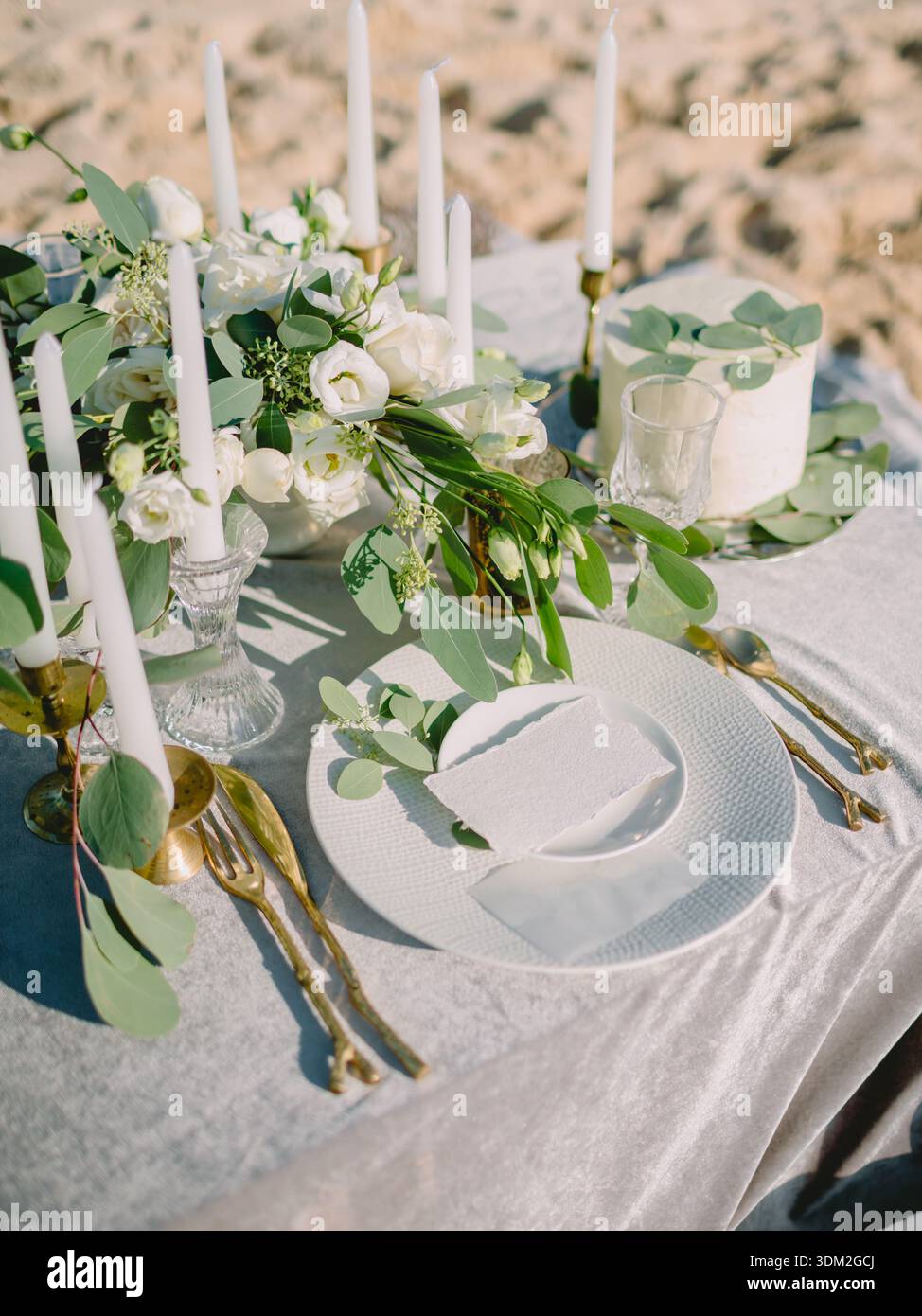 Elegante tavolo da nozze all'aperto con fiori bianchi, candele e torta sulla spiaggia sabbiosa, romantico ambiente da festa di lusso. Foto Stock
