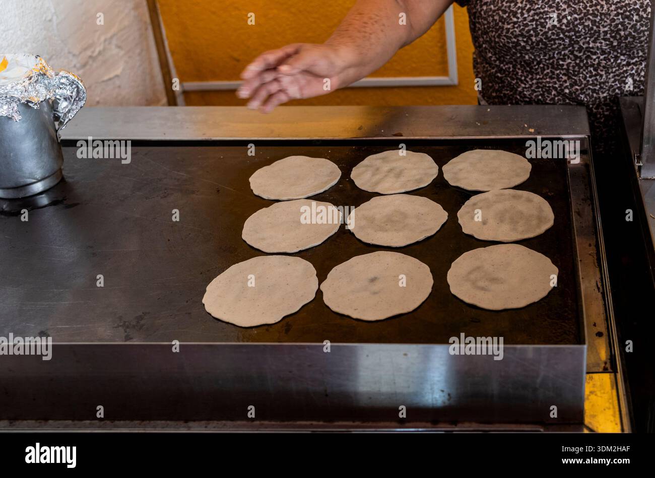 Tradizionale donna messicana che mette a mano tortillas di mais fresche sulla piastra calda. Autentica cucina comal. Foto Stock